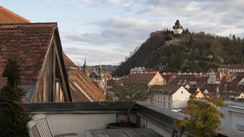 Graz hotel terrace overlooking red rooftops and the Schlossberg clock tower
