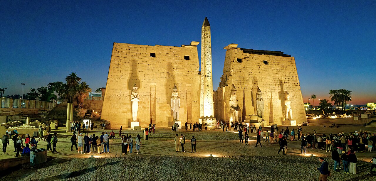 Illuminated entrance pylons, statues and obelisk at Luxor Temple at dusk