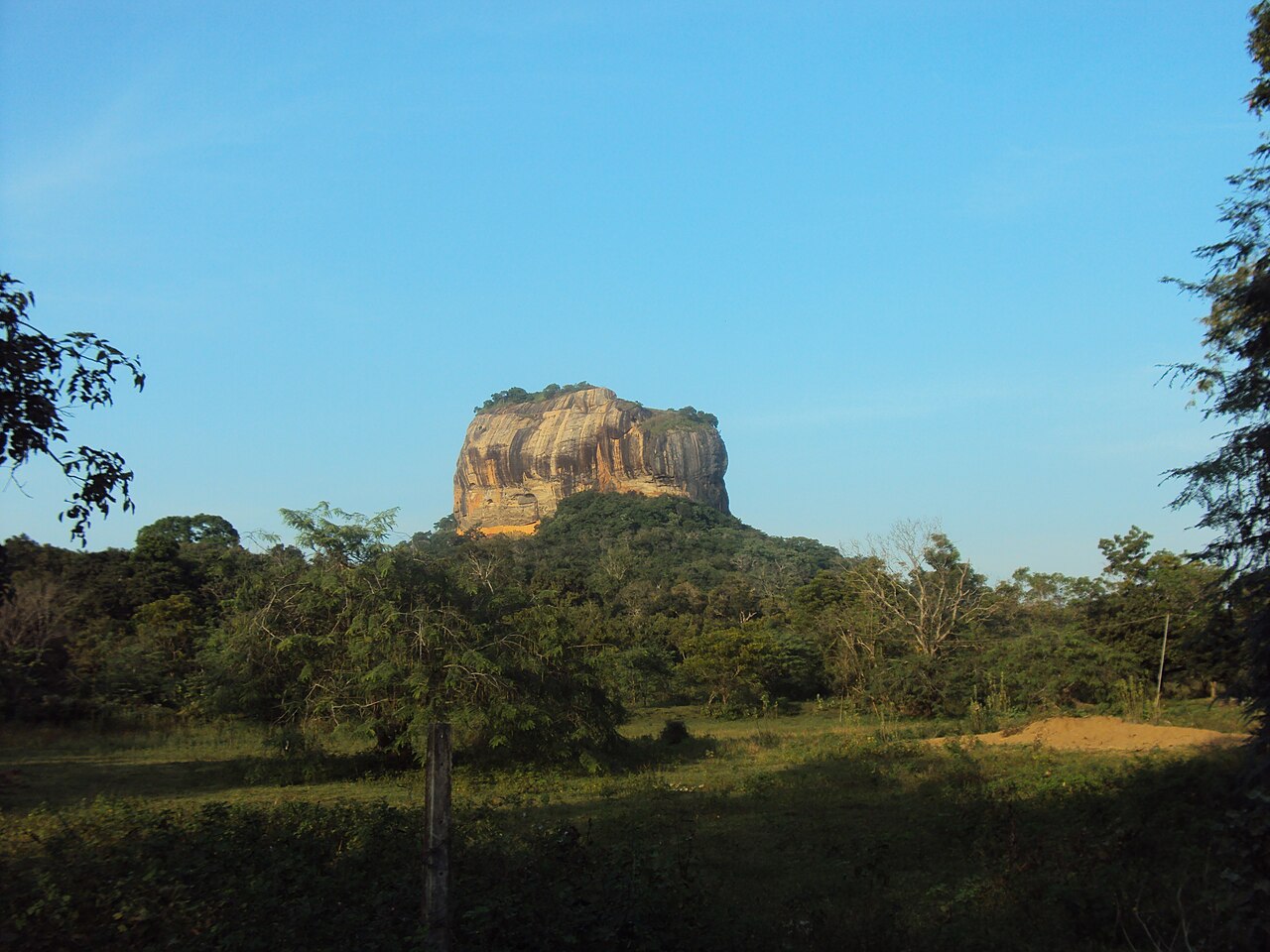 Sigiriya Rock rising above trees beneath a blue sky